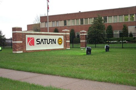 自動車工場の建物の前に広がる芝生に、サターンの会社ロゴの入った塀が見えてます。