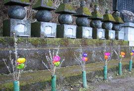 苔むした墓石が並び、その前に一輪挿しの花をいけた花瓶がそれぞれ供えられています。
