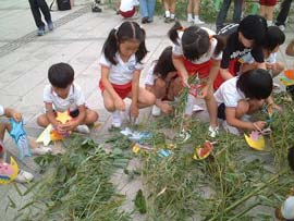 A group of children attach colored paper to bamboo branches, which are lying on the ground