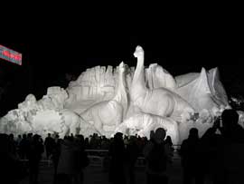 A snow sculpture of a dinosaur is lit up at night