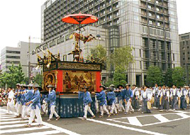 People in matching traditional attire pull a float down the street,  in front of an office building