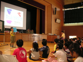 a group of students in a gym listen to a classmate's presentation