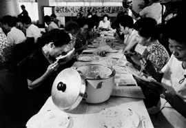 Many Japanese women eating rice at a banquet table.