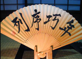 A close-up of a hand fan that contains Japanese writing on it.