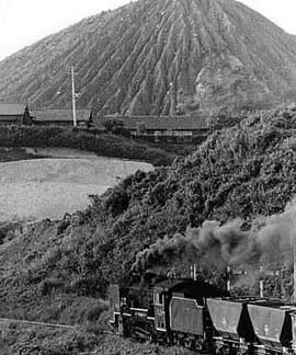 ボタ山を背景にもうもうと煙を吐きながら蒸気機関車が走っています。