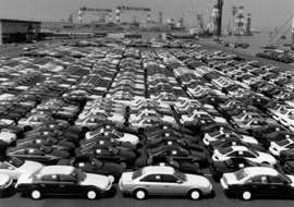 Rows of automobiles stretch across a wharf ready for export