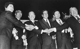 自民党以外の政治指導者6人が笑顔で互いに手を取り合っています。