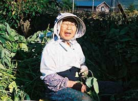 高齢の女性が笑顔で畑仕事をしています。