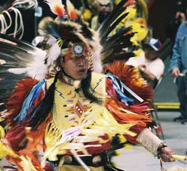 赤、黄色、青などの色鮮やかな羽根で作られた衣装と装飾品に身をまとい、男性が踊っています。
