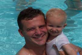 A man holds a small child while standig in pool.