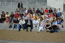 30数人の高校生がスーツを着た議員を囲み、国会議事堂の階段に座って記念撮影をしています。