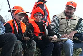 ２人の男の子と男性がおそろいのオレンジのベストを着て銃を持っています。