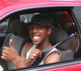 赤い車の中に、若いドライバーが運転席に座って大きな笑顔を見せています。