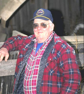A man stands next to a wood post inside his barn.