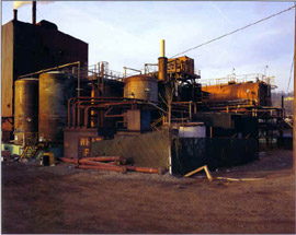 倒産した企業の工場なのか、赤茶けた金属製のタンクなどの前に、パイプなどが放置されています。