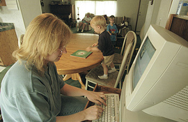 A woman works at a computer while her kids play.