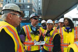 Group with masks and hardhats talk under a bridge