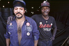 黒人の労働者が白人の同僚の肩に手をかけ、二人で微笑んでいます。